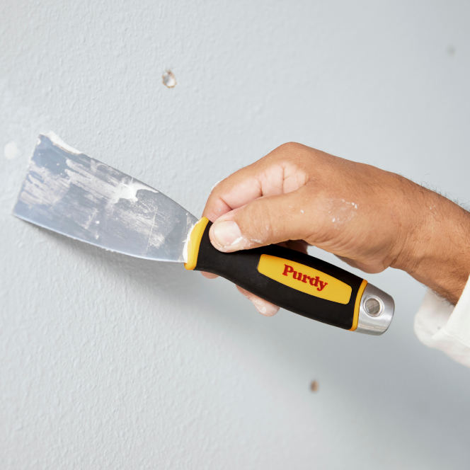 Pintor llenando agujeros en la pared con una espátula Purdy