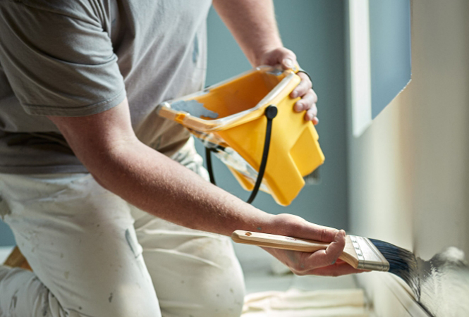 Professional painter cutting in around wall edges with a brush.