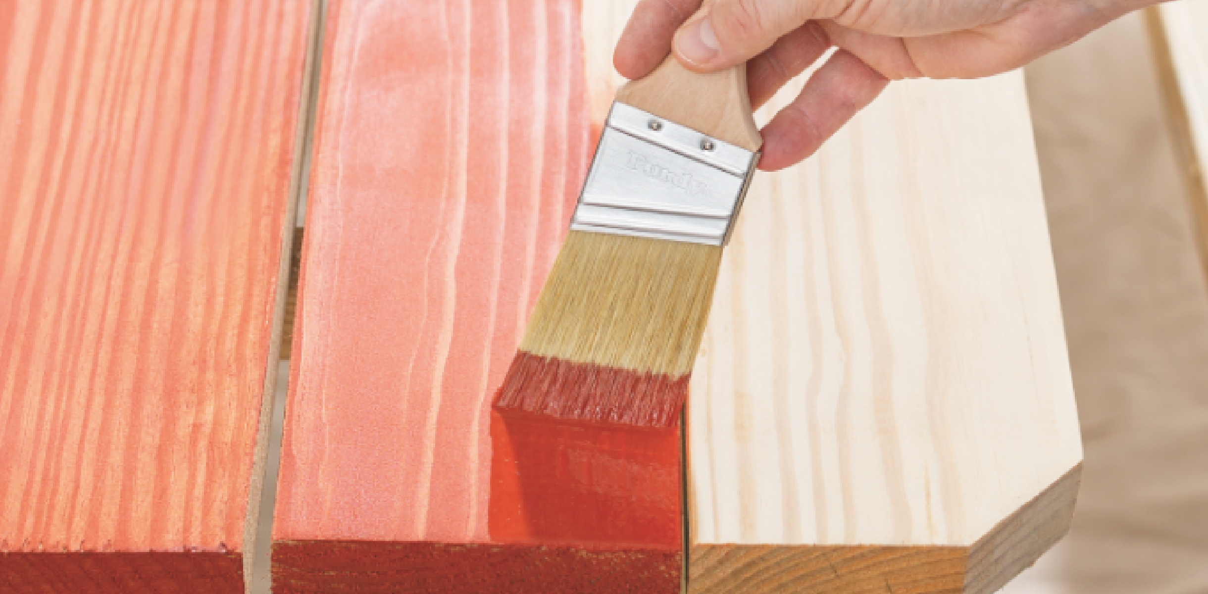 Painting a wood deck with a vibrant red stain using a natural bristle brush.