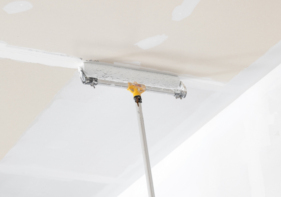 Painting a ceiling with a large roller and an extension pole.