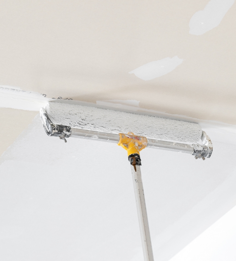 Painting a ceiling with a large roller and an extension pole.