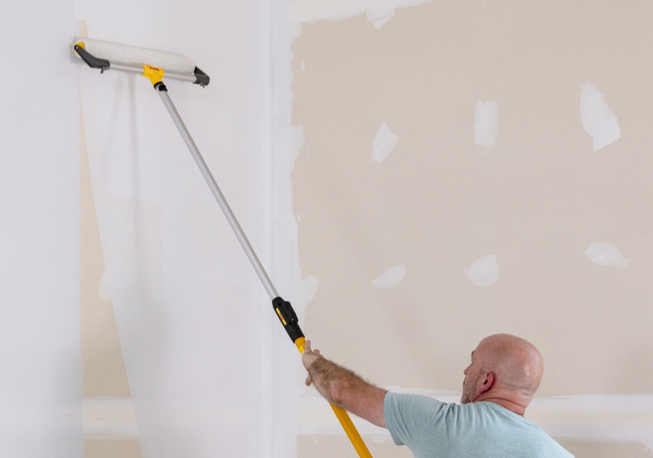 Pro painter rolling drywall with an eighteen-inch roller frame and extension pole.