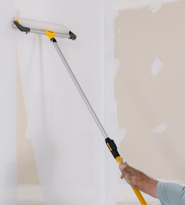 Pro painter rolling drywall with an eighteen-inch roller frame and extension pole.