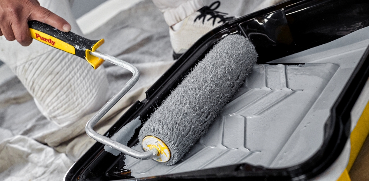 Pro painter rolling out light blue-gray paint in a paint tray.