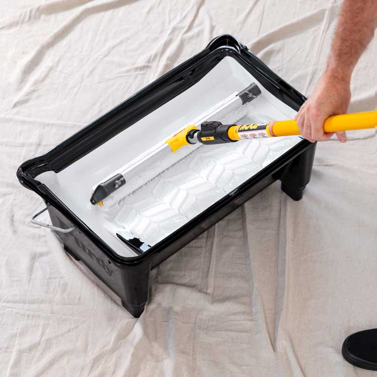 Pro painter rolling an oversized roller in a five-gallon bucket.