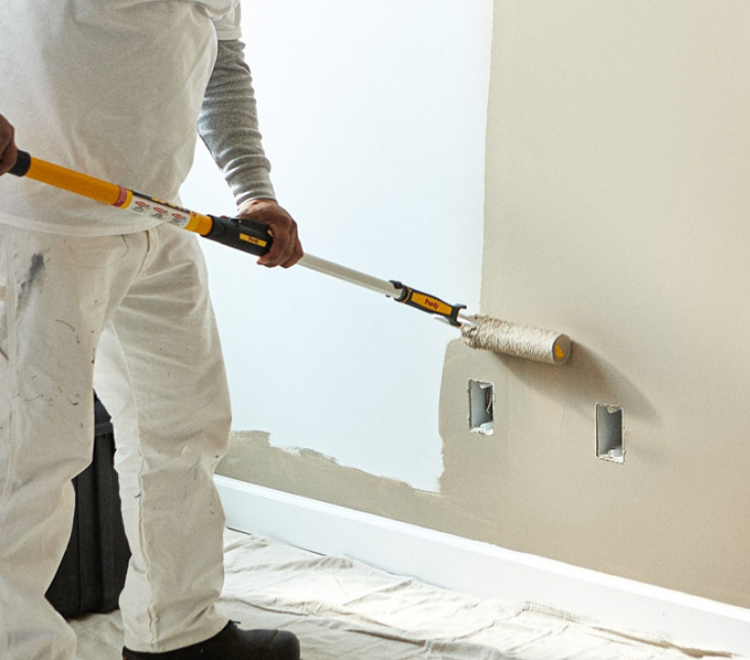 Professional painter painting an interior wall using a beige color.