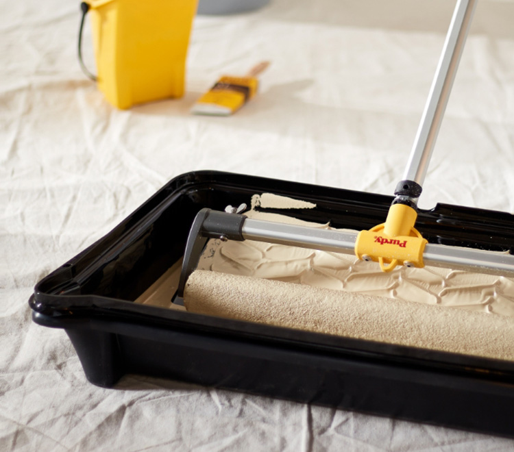 Painter rolling out paint in a large Nest paint tray using an eighteen-inch roller and an extension pole.