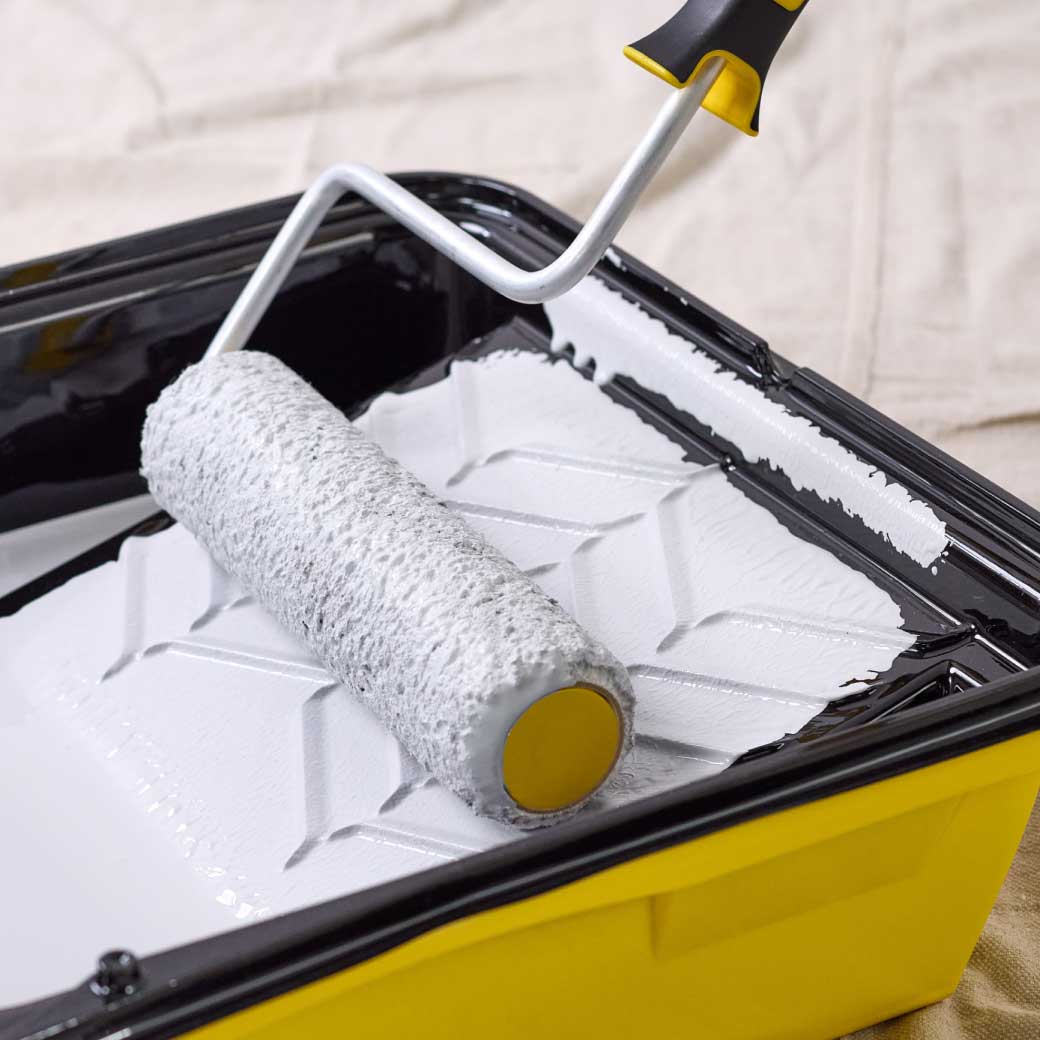 dipping a roller into a paint bucket and applying paint