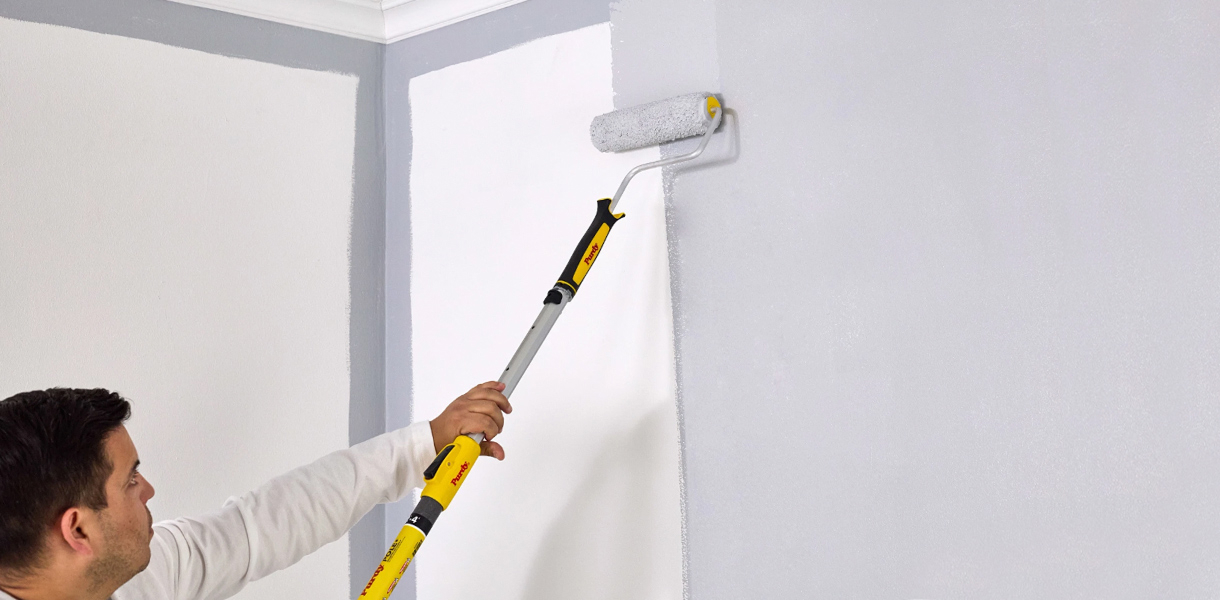 Professional Painter rolling paint on a wall with a Purdy roller, cover and pole.