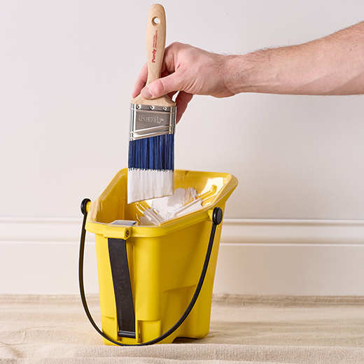 dipping a brush into a paint bucket