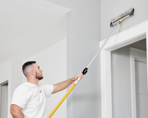 Pro rolling paint on a wall with a large roller.