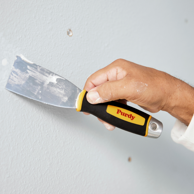 Painter filling holes in the wall with a Purdy putty knife.