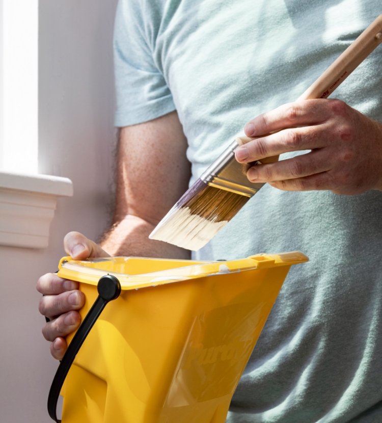 Pintor profesional con una brocha y un balde Purdy cerca de una ventana