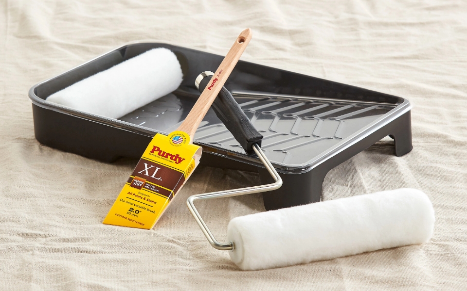 Purdy brush, roller and a paint tray on drop cloth.